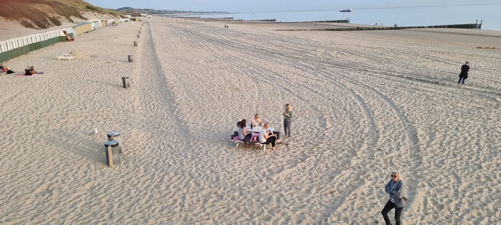 Breiter Sandstrand von Zoutelande, links eine Reihe bunter Strandhäuschen unter den Dünen, rechts die Buhnen im Wasser