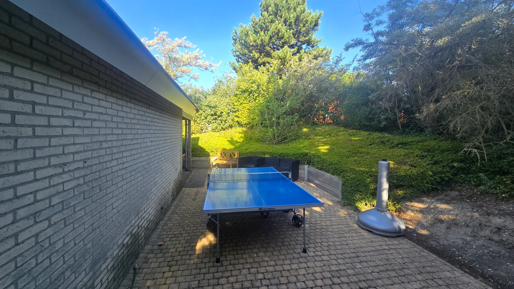 Der gepflasterte Platz an der Längsseite des Hauses, von Hecken und Kiefern umschlossen