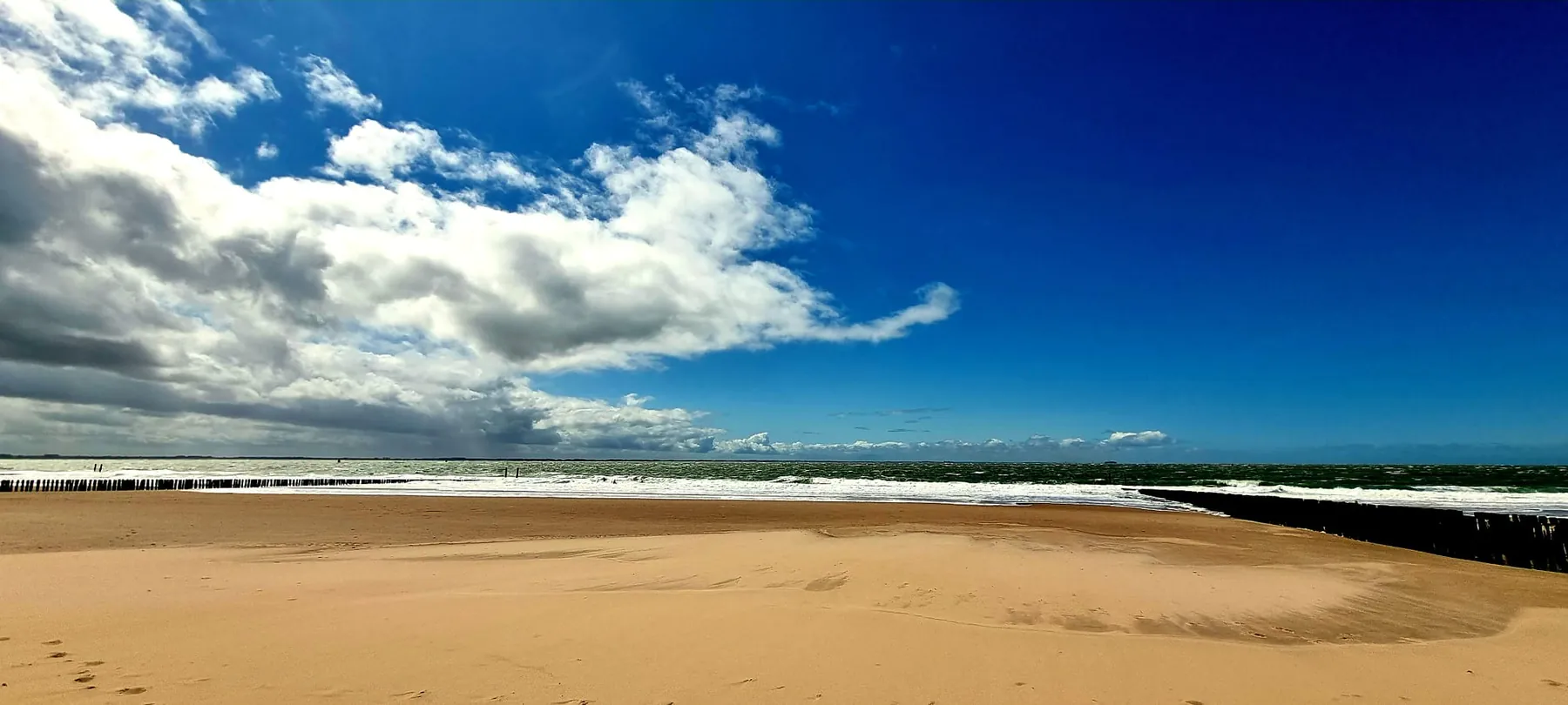 Breiter Sandstrand bei Zoutelande, links eine Regenwolkenwand über den Buhnen, rechts blauer Himmel über der Nordsee